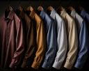 Premium men's shirts hanging on wooden hangers in rich colors including brown, blue and beige tones, showcasing high-quality fabric and craftsmanship